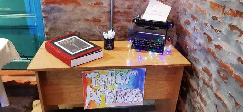 Escritorio con un libro y una máquina de escribir, más abajo un cartel Taller de arteterapia