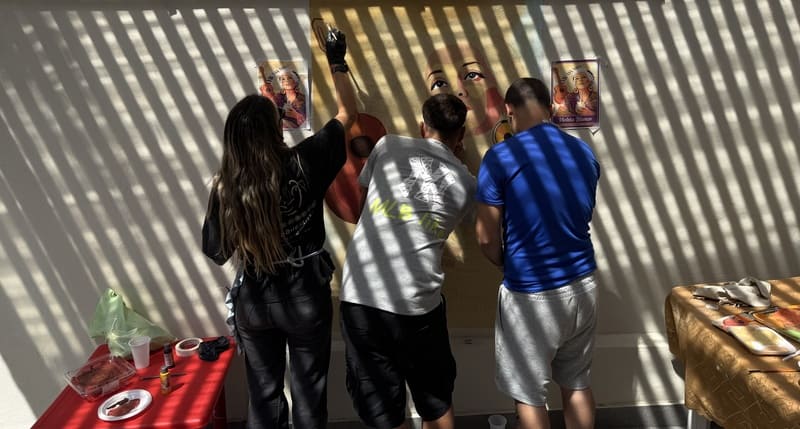 Dos jóvenes pintando el mural con una profesora